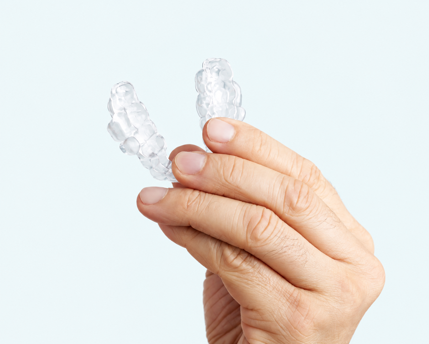 Example of a clear oral appliance held in a hand against a pale ice background