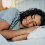 Curly-haired Black woman sleeps soundly on her side in bed after sleep apnea treatment