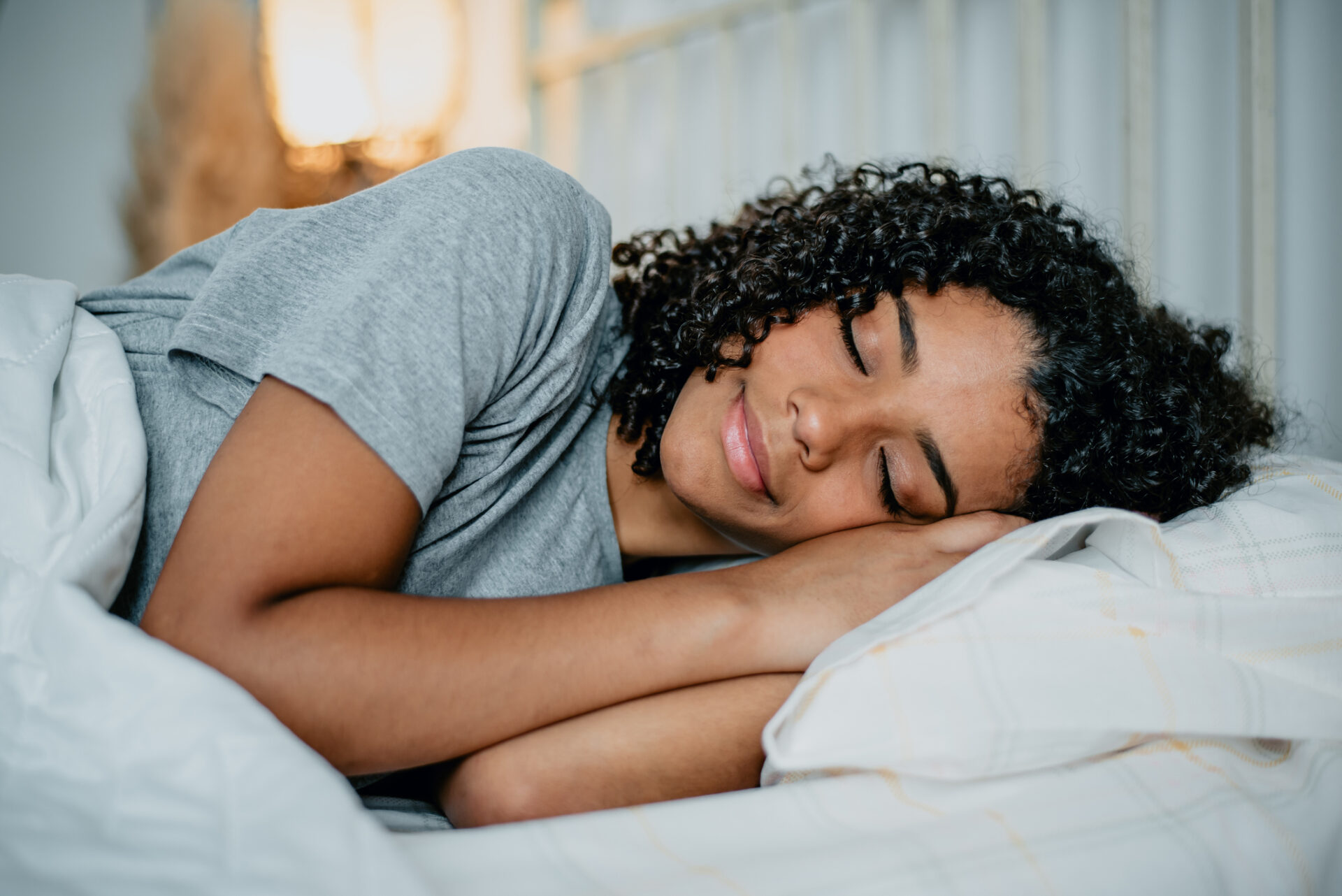 Curly-haired Black woman sleeps soundly on her side in bed after sleep apnea treatment