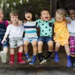 Group of smiling children sit next to each other on a bench outside