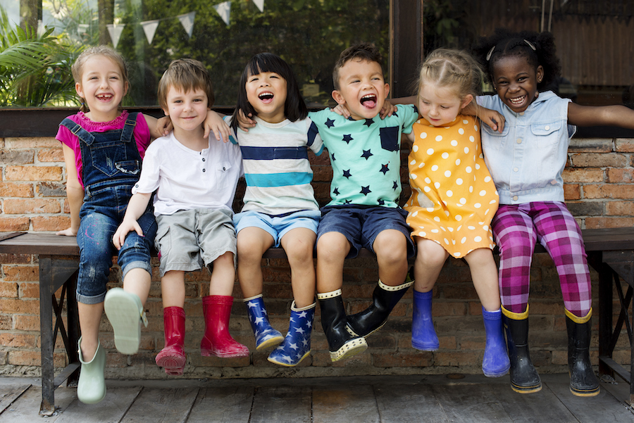 Group of smiling children sit next to each other on a bench outside
