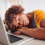 Black woman in a yellow shirt falls asleep on her laptop due to daytime sleepiness from an untreated sleep disorder