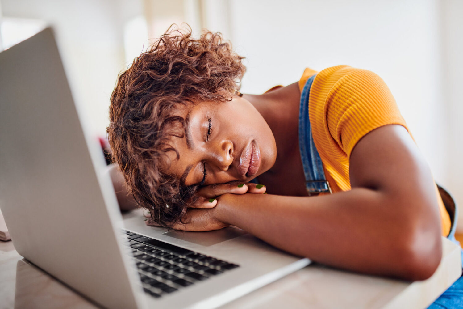Black woman in a yellow shirt falls asleep on her laptop due to daytime sleepiness from an untreated sleep disorder