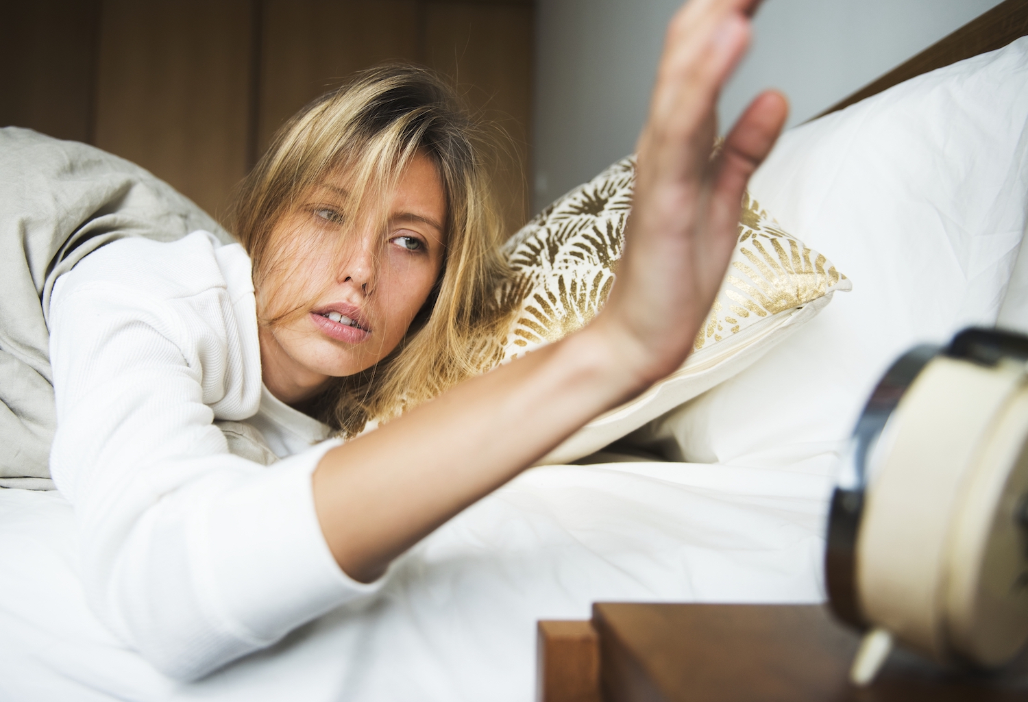 A blonde woman sleepily turns off her alarm clock