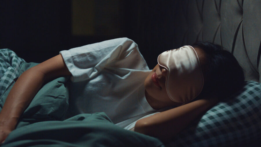 closeup of a woman sleeping in a dark room while wearing an eye mask