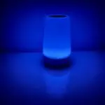 Closeup of a white noise sound machine with a blue glow on a nightstand