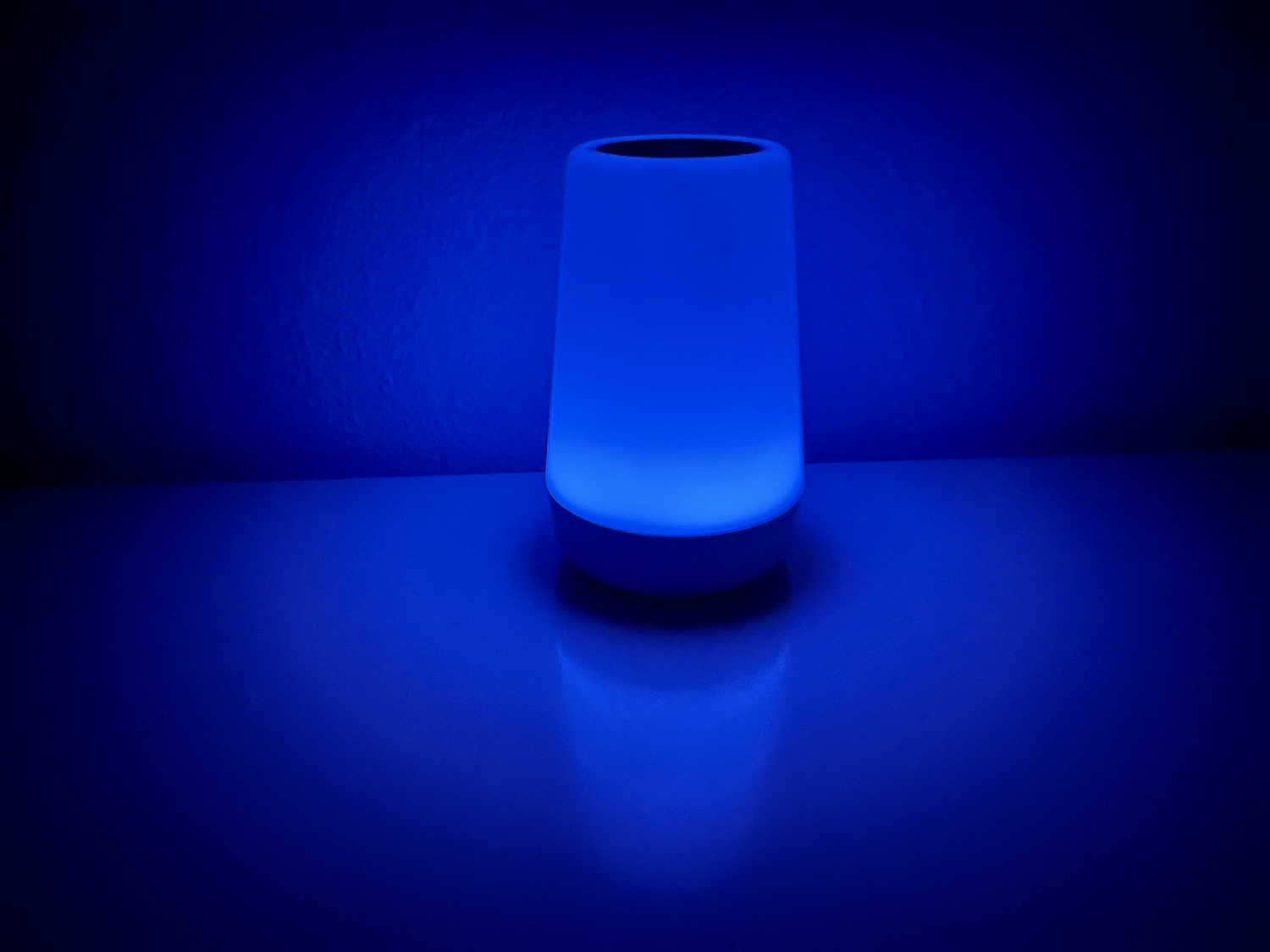 Closeup of a white noise sound machine with a blue glow on a nightstand